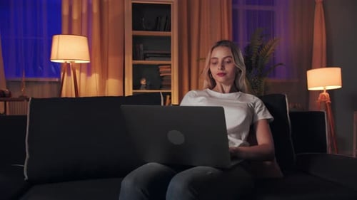 Young Woman Using Laptop on Couch at Night