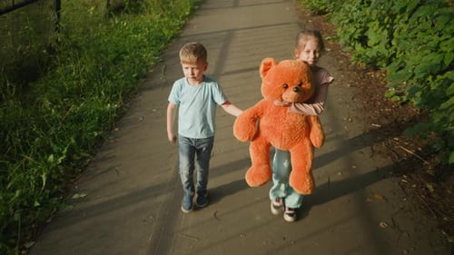 Little Girl and Brother Walking with Teddy Bear As Boy Looks Back on Path