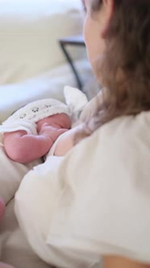 Woman Holding Newborn Baby in a White Bedroom