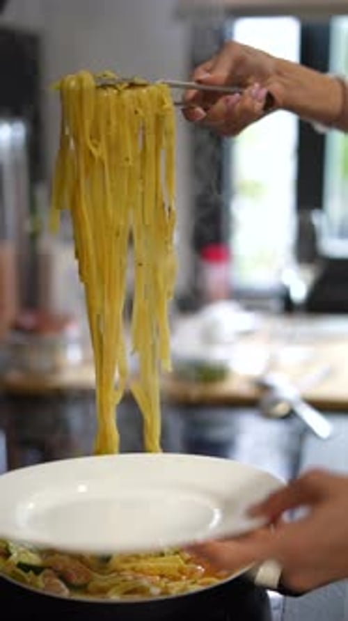 A Person is Skillfully Using Tongs to Serve Delicious Spaghetti Pasta in the Kitchen