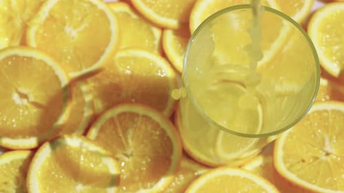Pouring Orange Juice into Glass Surrounded by Slices