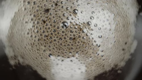 Coffee foam and bubbles spin in the cup as the camera zooms out. Macro shooting, slow motion