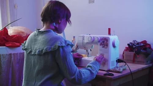 A Girl Sews on a Sewing Machine in the Blue Lighting of the House