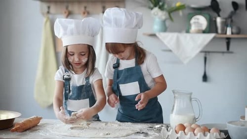 Two kids in white chef uniform making forms from dough on the kitchen