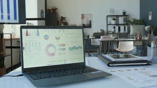 Laptop Displaying Financial Charts on Desk in Modern Office