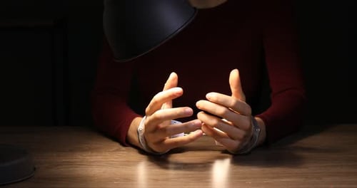 Hands in Handcuffs on Wooden Table Under Desk Lamp