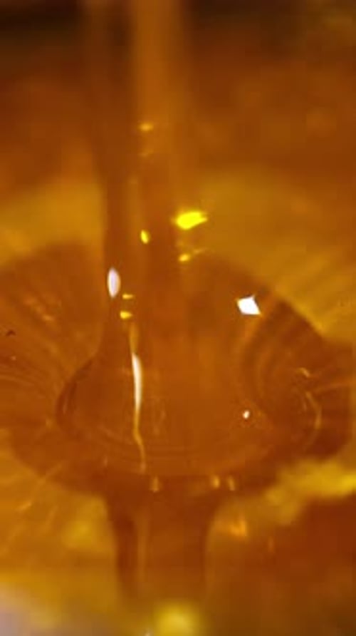 Unfiltered freshly extracted honey being poured onto metal sieve.
