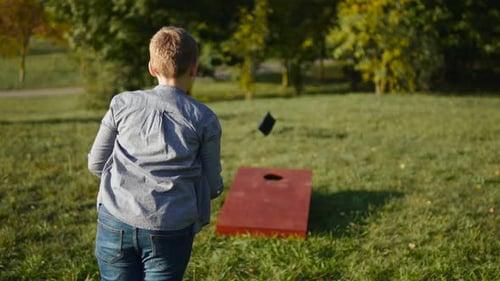 Boy Throws Bean Bag at Cornhole and Hits Target