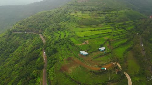 Aerial view of ghat road in Panchgani with vehicles driving through green hills under monsoon sky