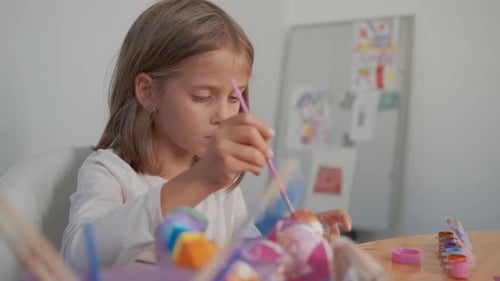 Seven Year Old Girl Painting with Brushes and Paints at Table