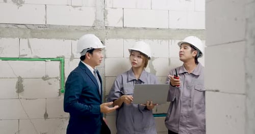 Asian male manager gestures beside female engineer using laptop and worker holding tool, leading