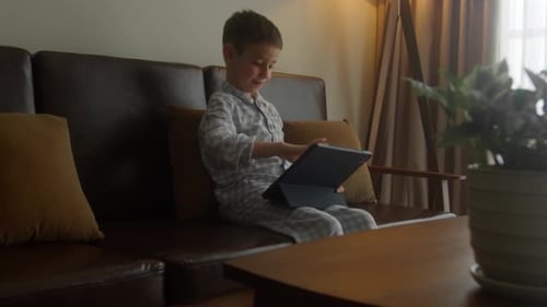 The Boy Sits on the Bed Playing or Watching a Movie Over the Internet Using a Tablet The Child