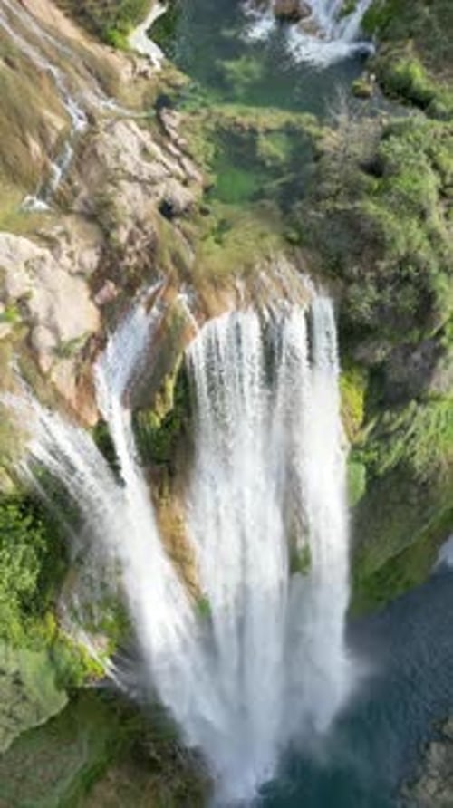 Aerial drone view of Tamul Waterfall cascading down green cliffs into a turquoise pool below. Vertic