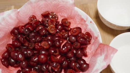 In a plate with a red-stained napkin, there are pitted cherry halves, top view.