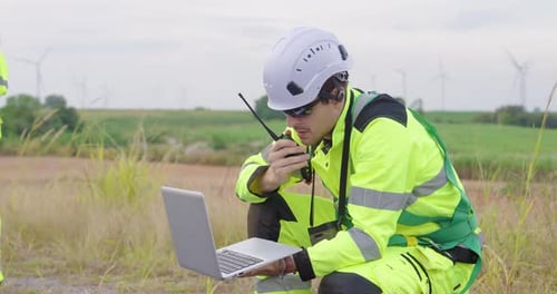 Ingenieur im Schutzanzug benutzt langsam den Laptop zur Überwachung der Windenergie, kommuniziert mit dem Team,