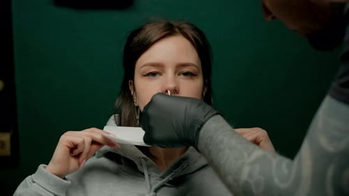Interior de un estudio de piercings: el maestro de piercings hace un piercing para una niña, piercing para el tabique nasal