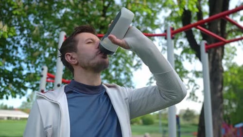 Man Drinks Water During Workout in the Park