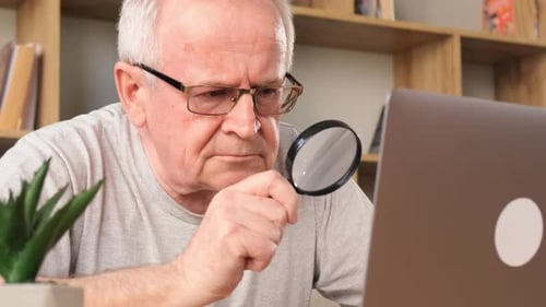Senior Man Using Magnifying Glass on Laptop