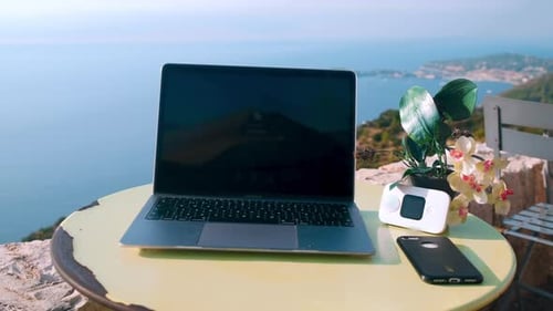 Foto de perto do local de trabalho ao ar livre com laptop e smartphone na mesa e bela paisagem oceânica