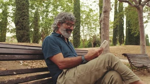 Smiling elderly man using phone while sitting in park