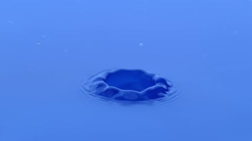 Blue water droplet creates ripples on water surface