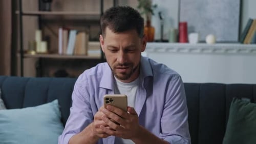 Attractive Smiling Happy Young Man Use Phone Sitting on Sofa at Home Communication Businessman