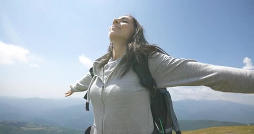 Close up of carefree happy female tourist with backpack is breathing deeply with open arms raised