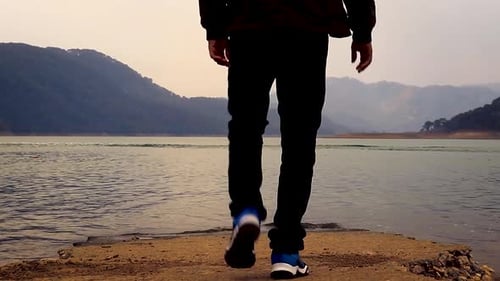 young man walking towards at lake shore at morning from low angle