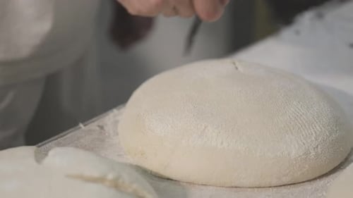 The process of making bread in a bakery. After proofing, the top of the bread is cut with knife.