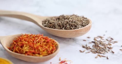 Different aromatic spices in wooden spoons on white marble table, closeup. Camera moving