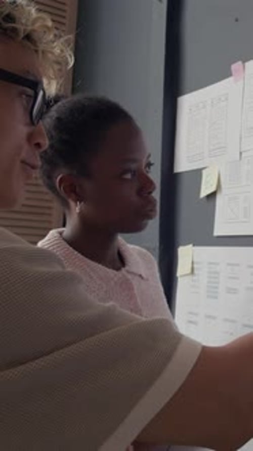 Vertical of Female UX Designer Discussing Mobile App UI on Wall with Colleague