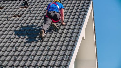 Professional male roofer climbs down the roof