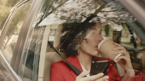 Woman in car using phone and drinking coffee