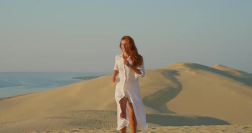 Beautiful Woman Runing in Long White Clothes Against the Backdrop of a Beautiful Sunset on Sand Dune