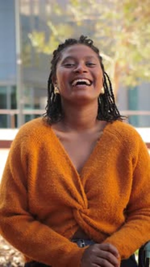 Joyeuse jeune femme souriante tout en se tenant debout avec confiance avec ses mains sur ses hanches à l'extérieur