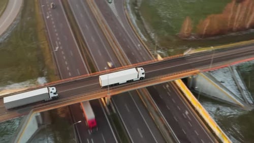 A truck drives over a bridge crossing a high-speed highway with heavy traffic