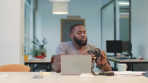 Man Inspects a Camera at an Office Desk