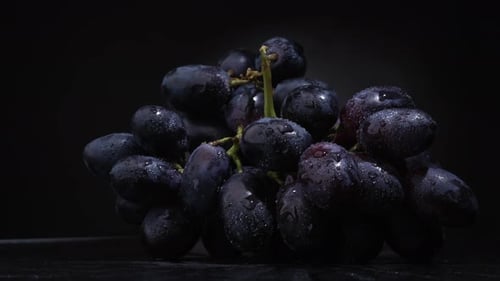 Rotating Wet Dark Grapes on a Black Surface