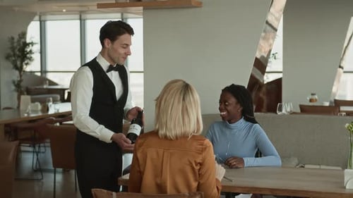 Young Server Offering Bottle of Fine Wine to Female Guests in Restaurant