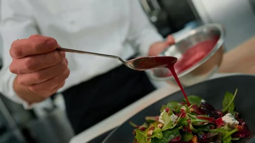 Professional kitchen the chef pours red sauce on the salad with pear and cheese mixes the ingredient