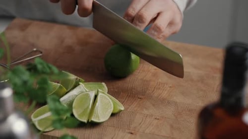 Young Male cutting a lime in half with sharp knife on wooden cutting board in kitchen at home. Close