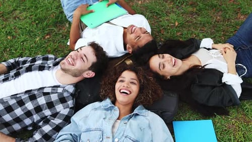 Diverse young multi-ethnic students lying on the grass of the university campus laughing