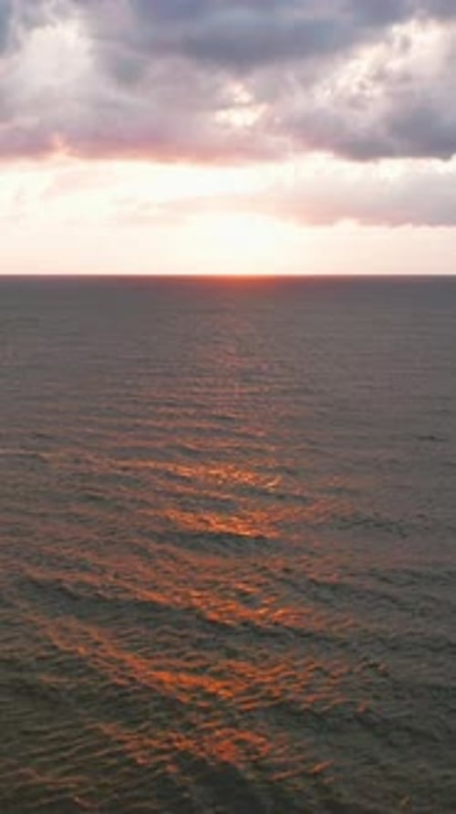 La lumière du coucher du soleil se reflète sur les vagues calmes de l'océan sous des nuages Théâtraux