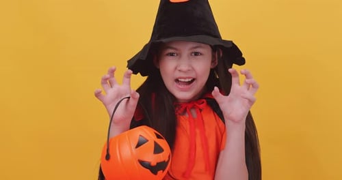 Cute little girl wearing a witch costume to celebrate Halloween on yellow background.