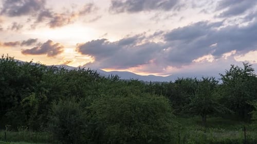 Time lapse of moving clouds over the green mountains with changing colors of the sky.