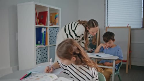 Thoughtful Pupil Doing Class Work at Cabinet Desk Woman Teacher Helping Boy