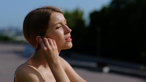 Caucasian Young Happy Woman Putting Wireless Earphones Into Ears and Listening to Music Outside