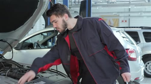 Mechanic Looks Under the Car Hood at the Car Service