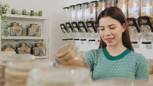 A young woman is shopping in refill store with reusable bag, zero-waste grocery.