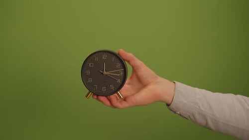 A Hand Holding a Round Clock is Showcased Against a Green Background Creating Contrast